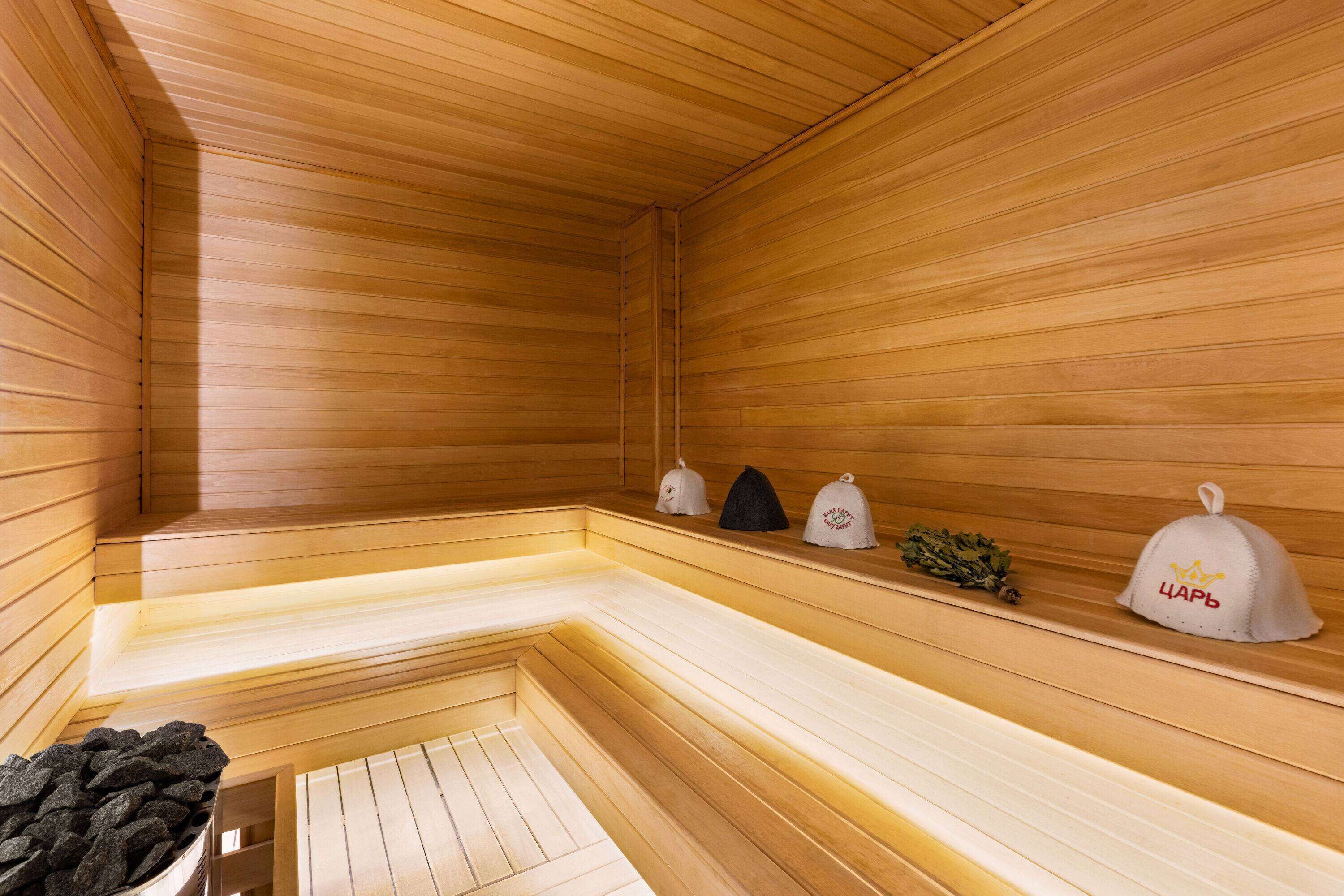 A sauna with wooden walls and benches, a bench with a towel, and three towels on a shelf.