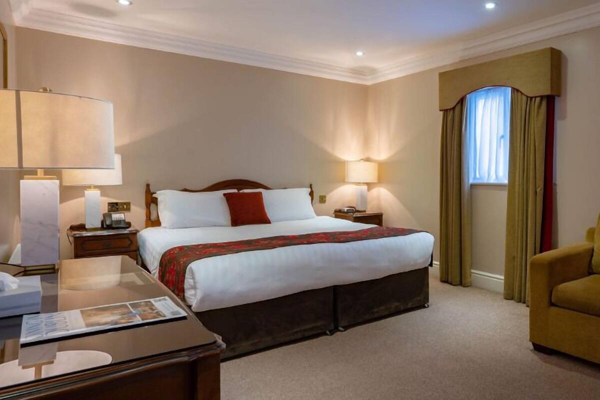 Une chambre d’hôtel avec un grand lit, deux lampes de chevet, un bureau avec une chaise, un canapé et un tableau encadré au mur.