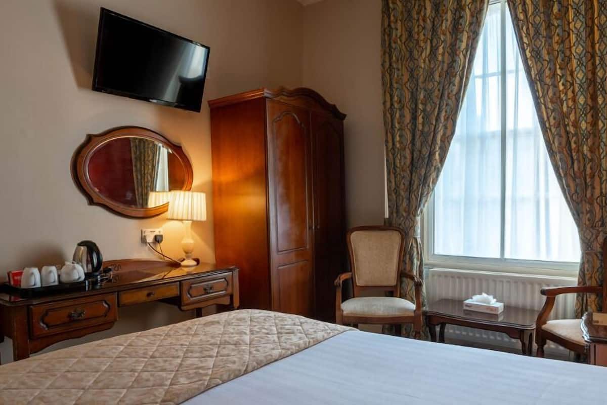 Une chambre d’hôtel comprenant un lit, un bureau avec un miroir, une armoire, une chaise et un téléviseur fixé au mur.