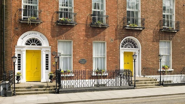 A brick building with two yellow doors, a white entrance, and a black wrought iron fence.