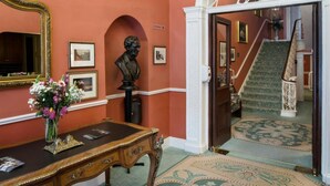 A grand hallway with a large mirror, a bust, and a staircase leading to another room.