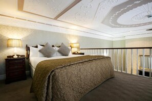 A bedroom with a bed, two bedside tables with lamps, a wooden headboard, and a balcony railing. - Harrington Hall (Dublin)