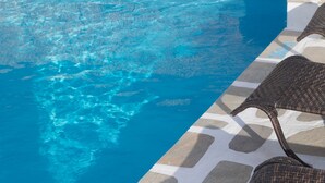 A swimming pool with clear blue water, surrounded by stone tiles and wicker lounge chairs. - Mare Naxia (Naxos)
