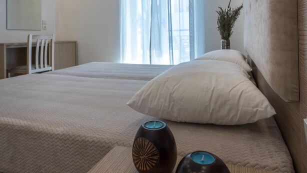 A modern hotel room with two beds, a desk, a chair, and a large window with curtains. - Mare Naxia (Naxos)