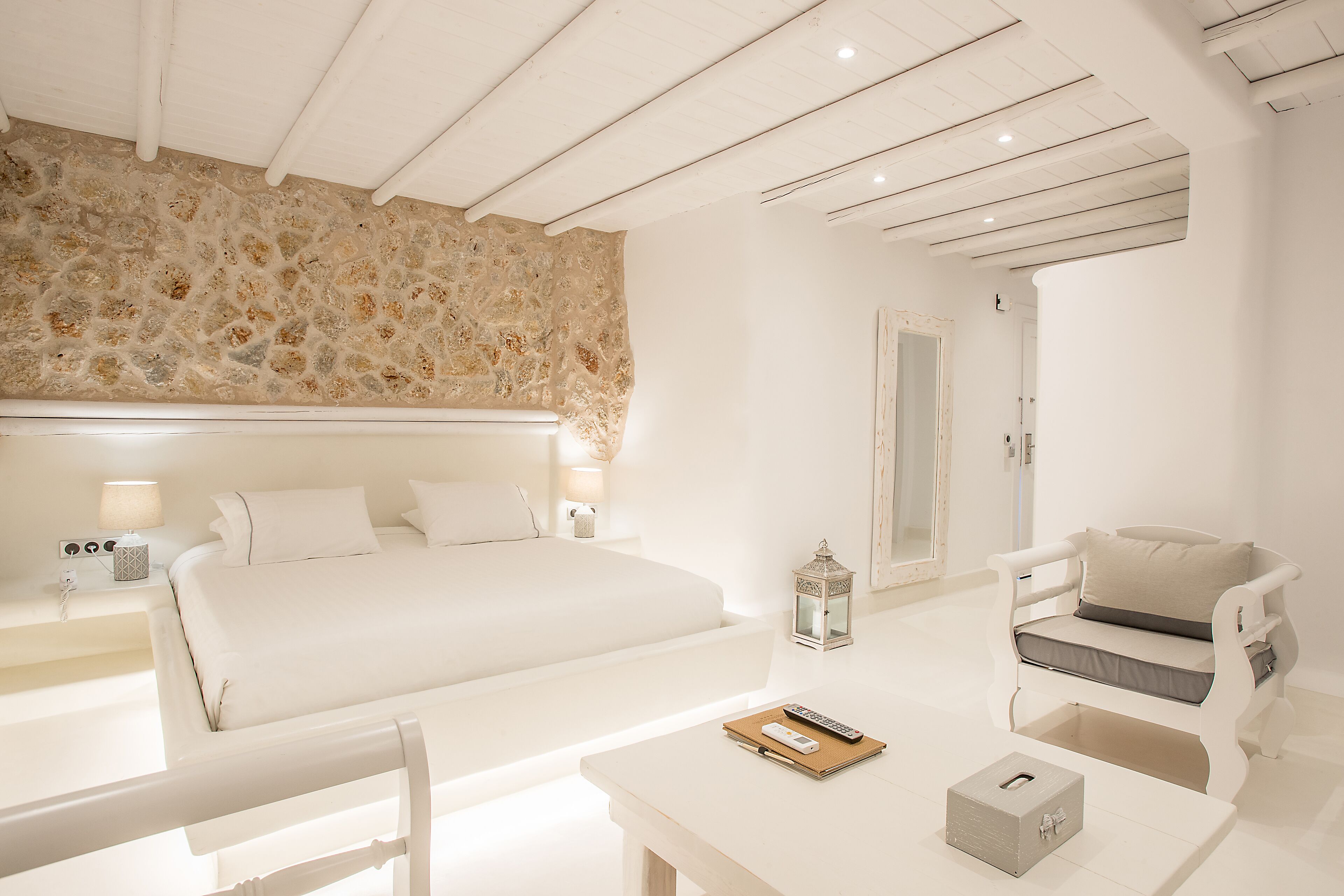 A bedroom with a large bed, bedside lamps, a nightstand, a small table with a remote control, a box, and a chair.