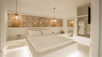 Une chambre moderne avec un grand lit, un mur d’accent en pierre et une coiffeuse intégrée dotée d’un miroir et de crochets pour les peignoirs.