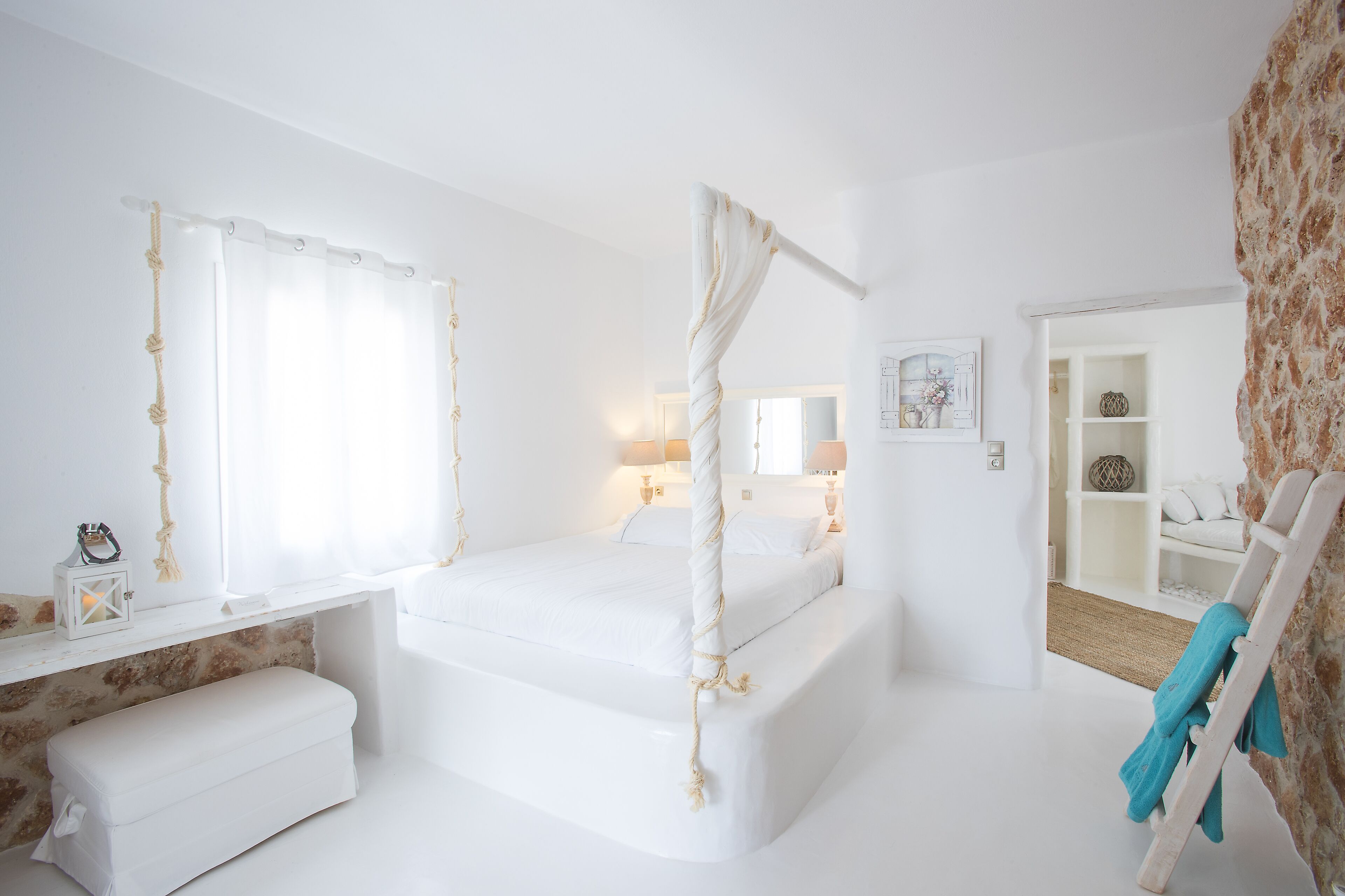A white bedroom with a four-poster bed, a bedside table, and a bench.