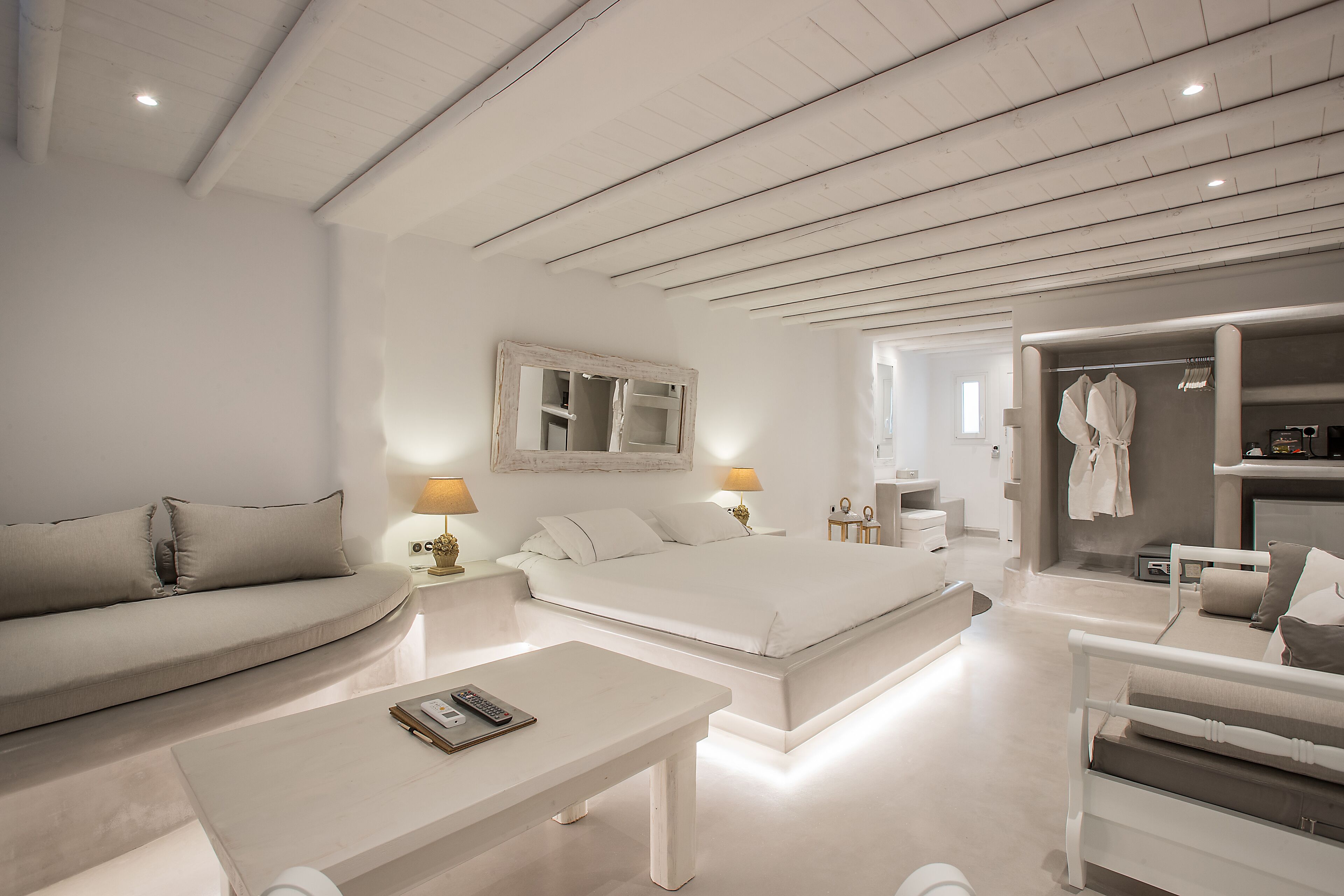 A modern bedroom with a large bed, a sofa, a bedside table, and a walk-in closet.