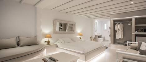 A modern bedroom with a large bed, a sofa, a bedside table, and a walk-in closet.