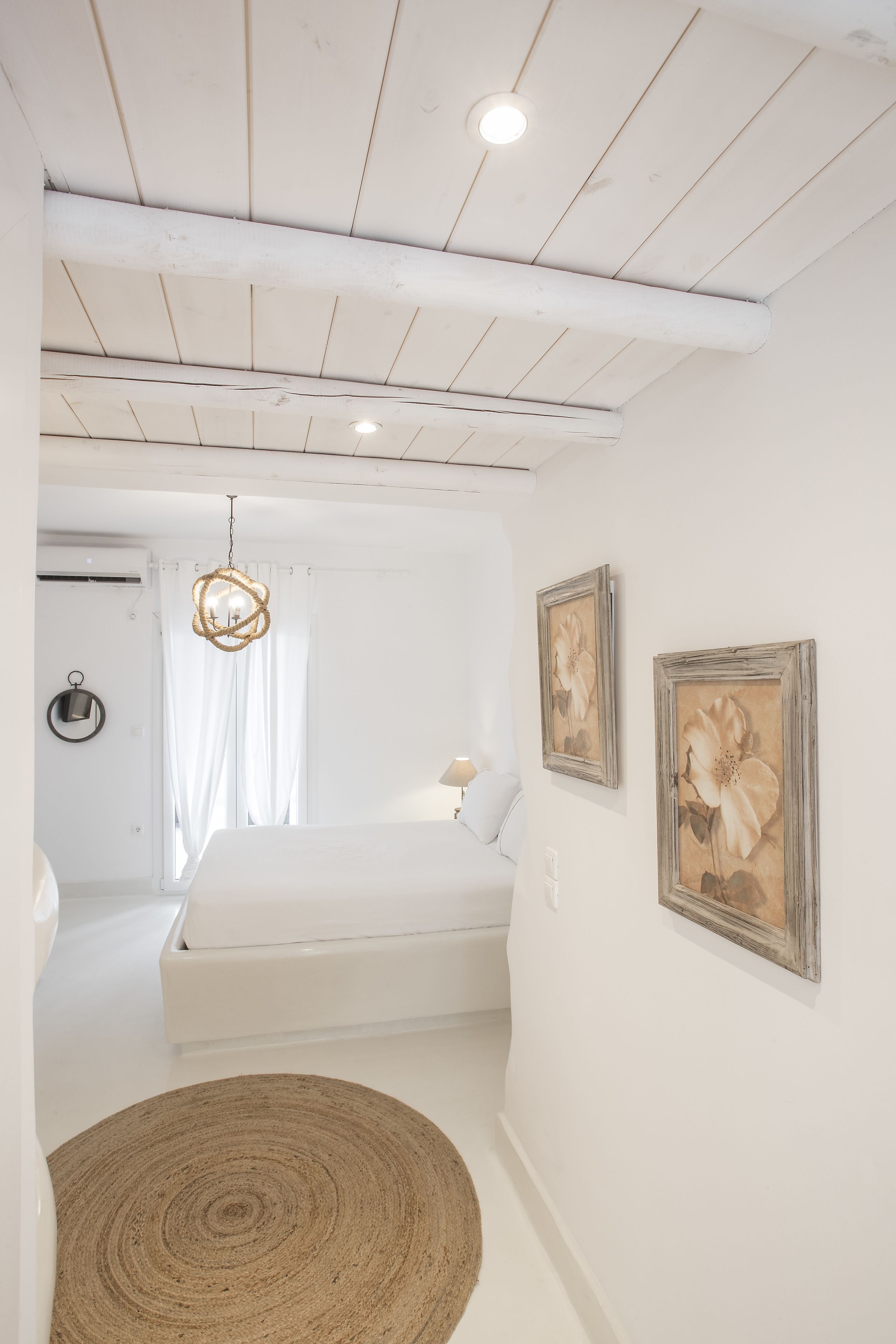 A bedroom with a bed, a round woven rug, a hanging light fixture, and two framed floral pictures on the wall.
