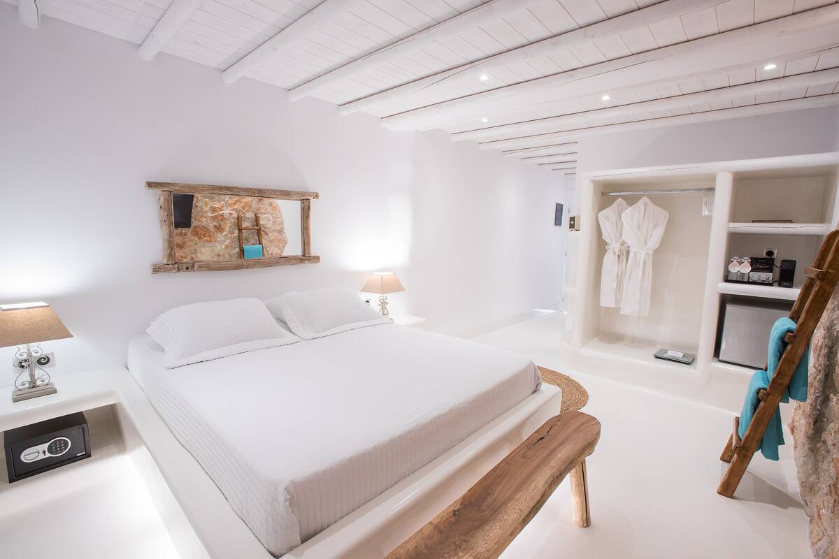 A modern bedroom with a large bed, bedside tables, a wooden bench, a wardrobe, and a mirror on the wall.