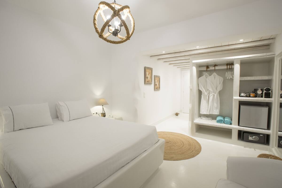 A modern bedroom with a large bed, a walk-in closet, and a unique chandelier.