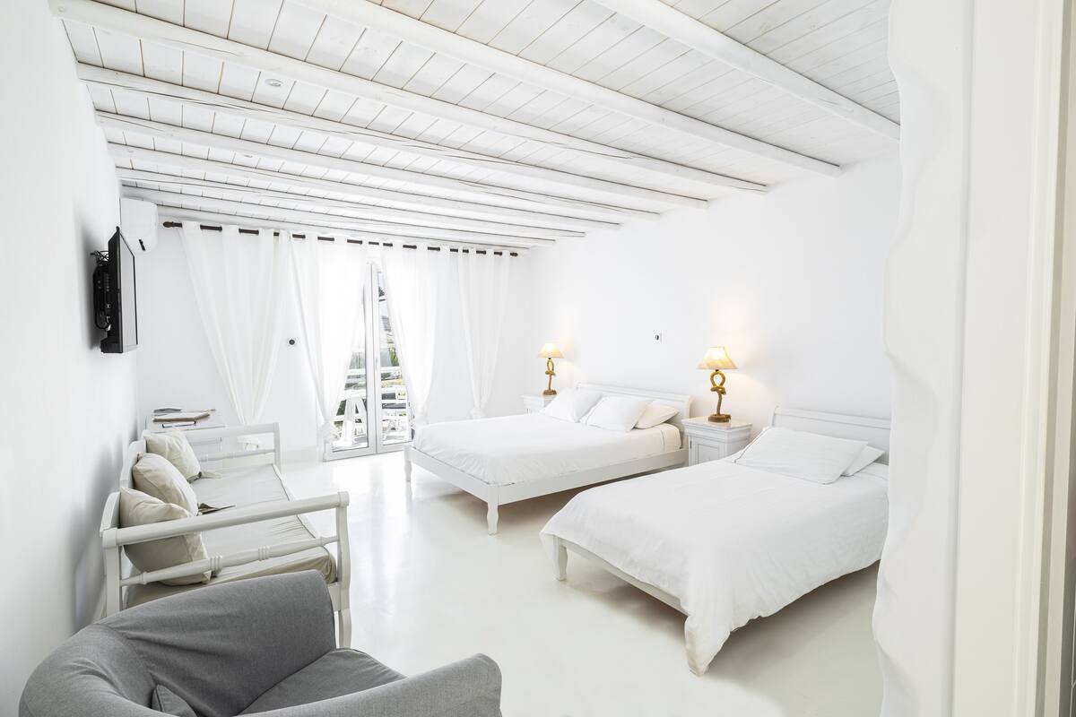A hotel room with two beds, a chair, a TV, and a balcony with a view.