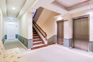 Un vestíbulo de hotel con una escalera de mármol, dos ascensores y un sofá.