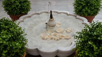 A fountain with water spouting from a central nozzle, surrounded by a scalloped edge basin.