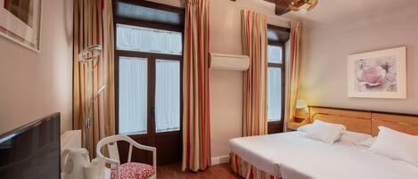 A hotel room with a bed, a desk with a computer, a chair, and a window with curtains.