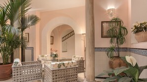 Un vestíbulo con una mesa de vidrio, sillas acolchadas, una planta en maceta grande y una lámpara de pared decorativa.