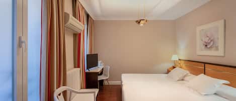 Una habitación de hotel con una cama, un escritorio con computadora, una silla y una ventana con cortinas.