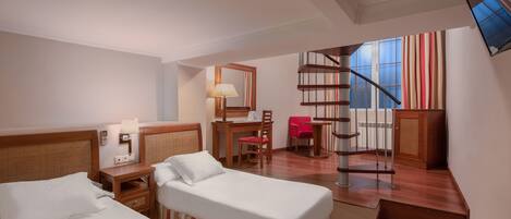 A hotel room with two beds, a desk, a chair, a lamp, and a spiral staircase leading to a balcony.