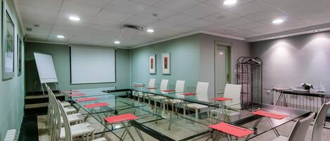 Une salle de conférence équipée d’une table en verre, de chaises blanches, d’un écran de projection et d’un tableau blanc.