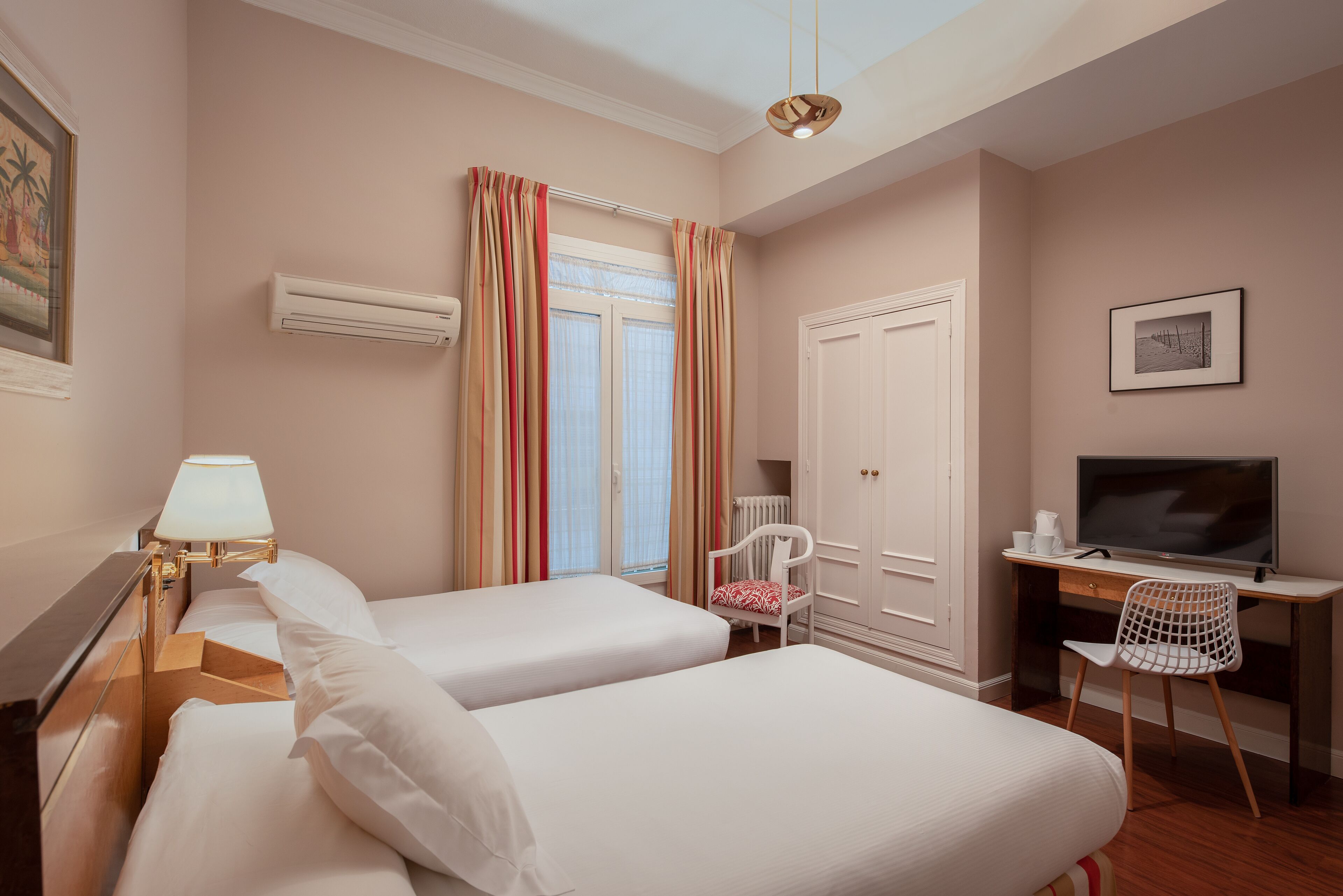 A hotel room with two beds, a desk with a chair, a television, and a window with curtains.