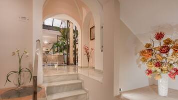 A staircase leading to a second floor with a view of a dining area and a large floral arrangement.