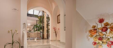 A staircase leading to a second floor with a view of a dining area and a large floral arrangement.
