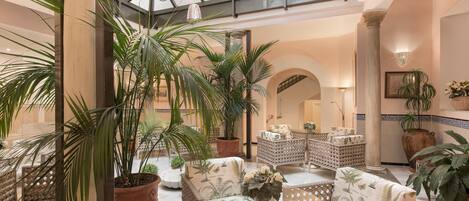 A spacious lobby with wicker furniture, potted plants, and a glass ceiling.