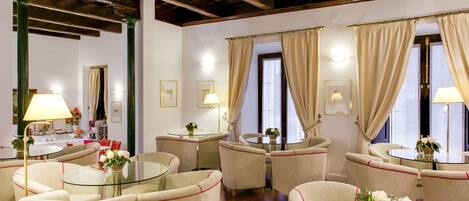 A room with a round glass table surrounded by beige upholstered chairs, a wooden ceiling, and beige curtains on the windows.