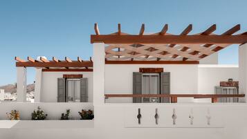 A white building with a wooden pergola, grey shutters, and a small balcony with potted plants.