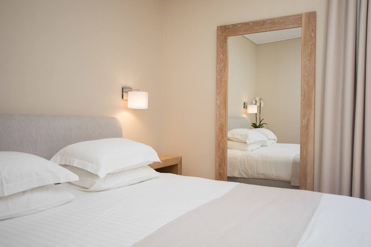 A hotel room with a large bed, a nightstand, a wall-mounted lamp, and a mirror.