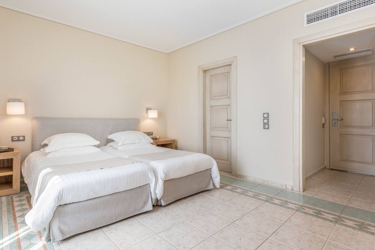 A double bed with a headboard, two bedside tables, a nightstand, a wall-mounted light, and a door with a handle.