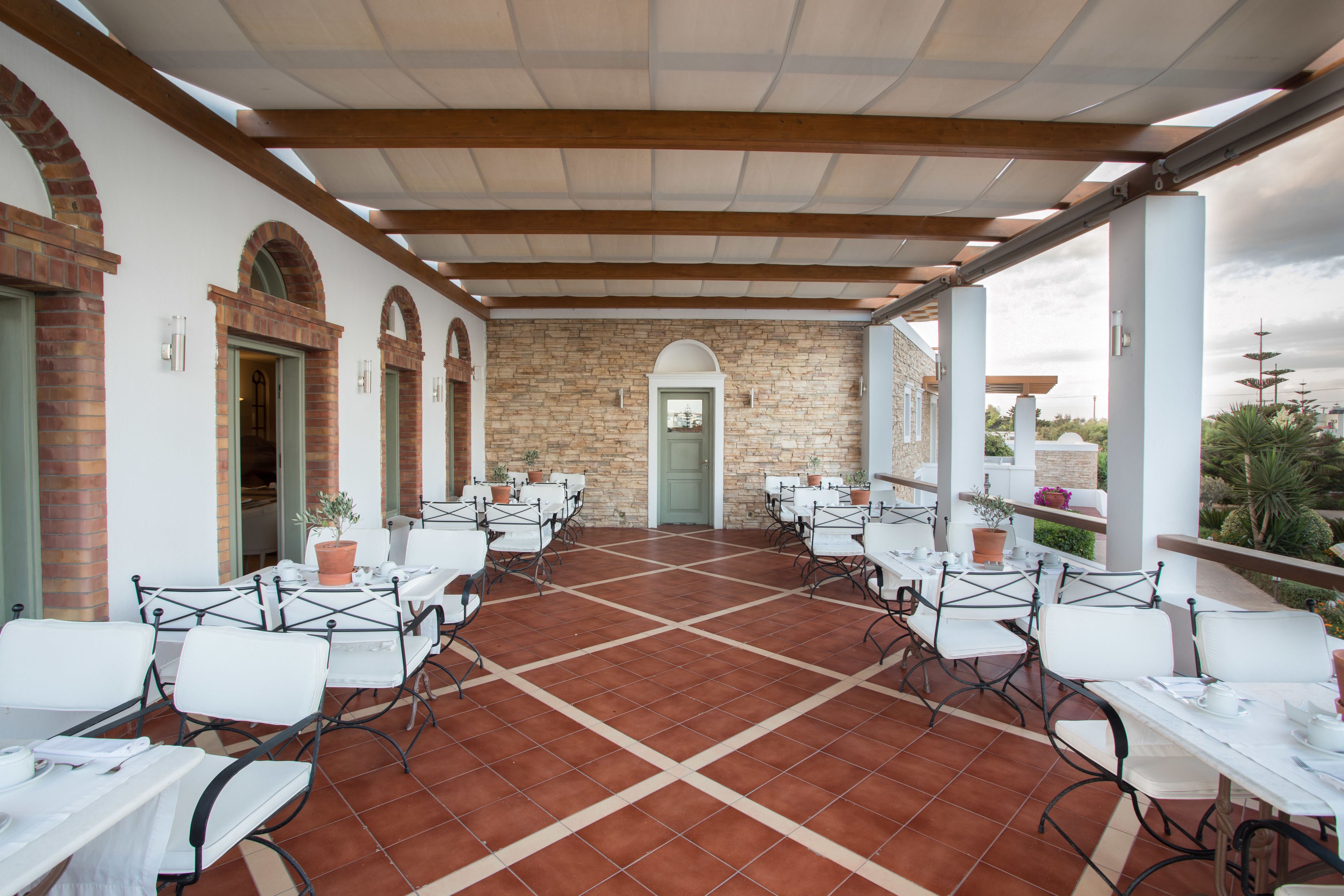 A covered outdoor patio with white tables and chairs, stone walls, and a view of the surrounding landscape.