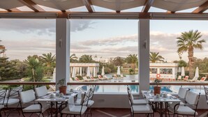 Un área de estar al aire libre con techo y vistas a la piscina, con mesas y sillas dispuestas para comer.