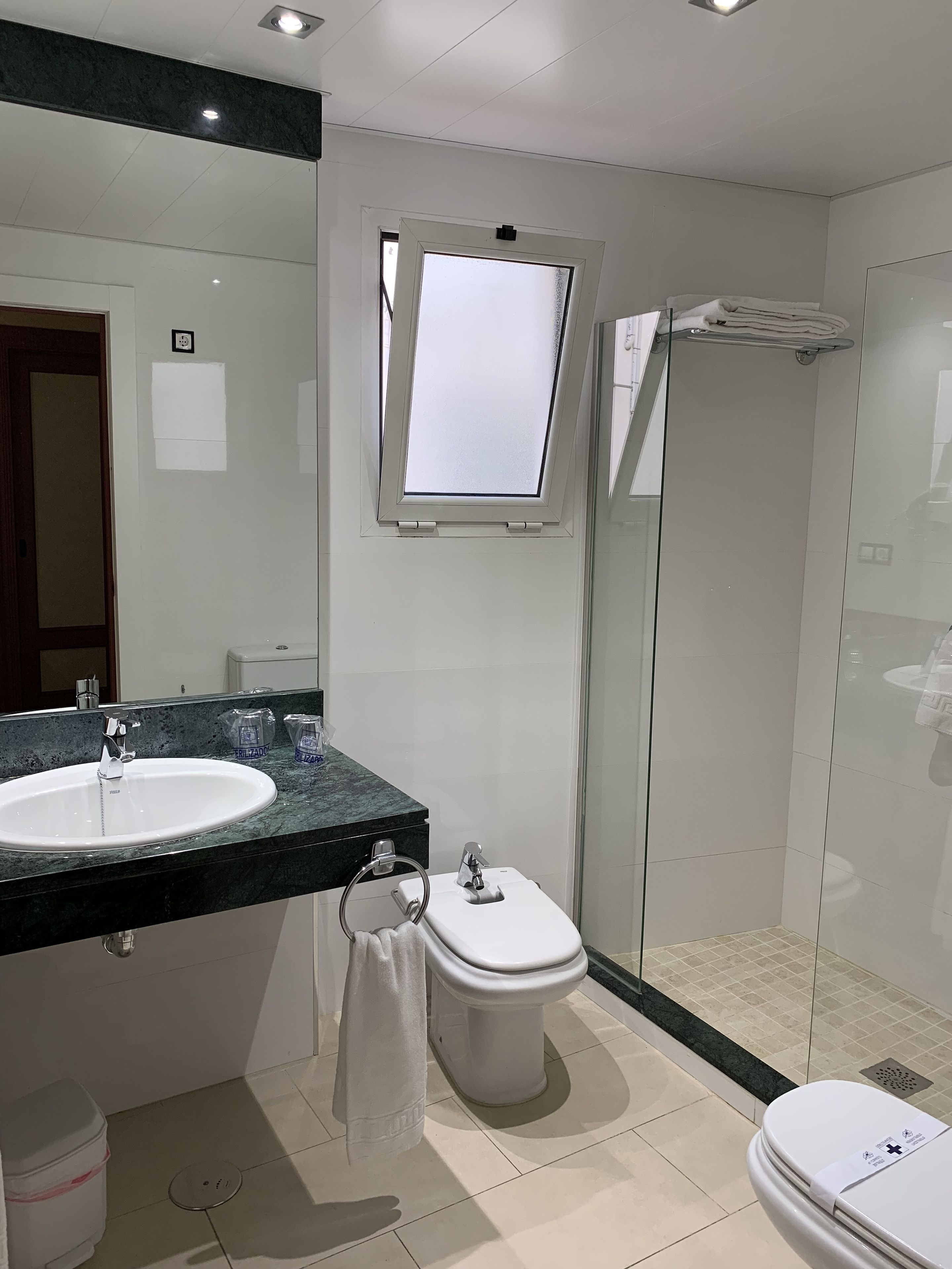 A modern bathroom with a large mirror, a sink, a toilet, and a shower enclosure.
