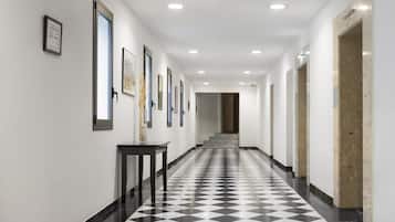 Un pasillo con piso a cuadros, obras de arte enmarcadas en las paredes y una escalera que sube a otro nivel.