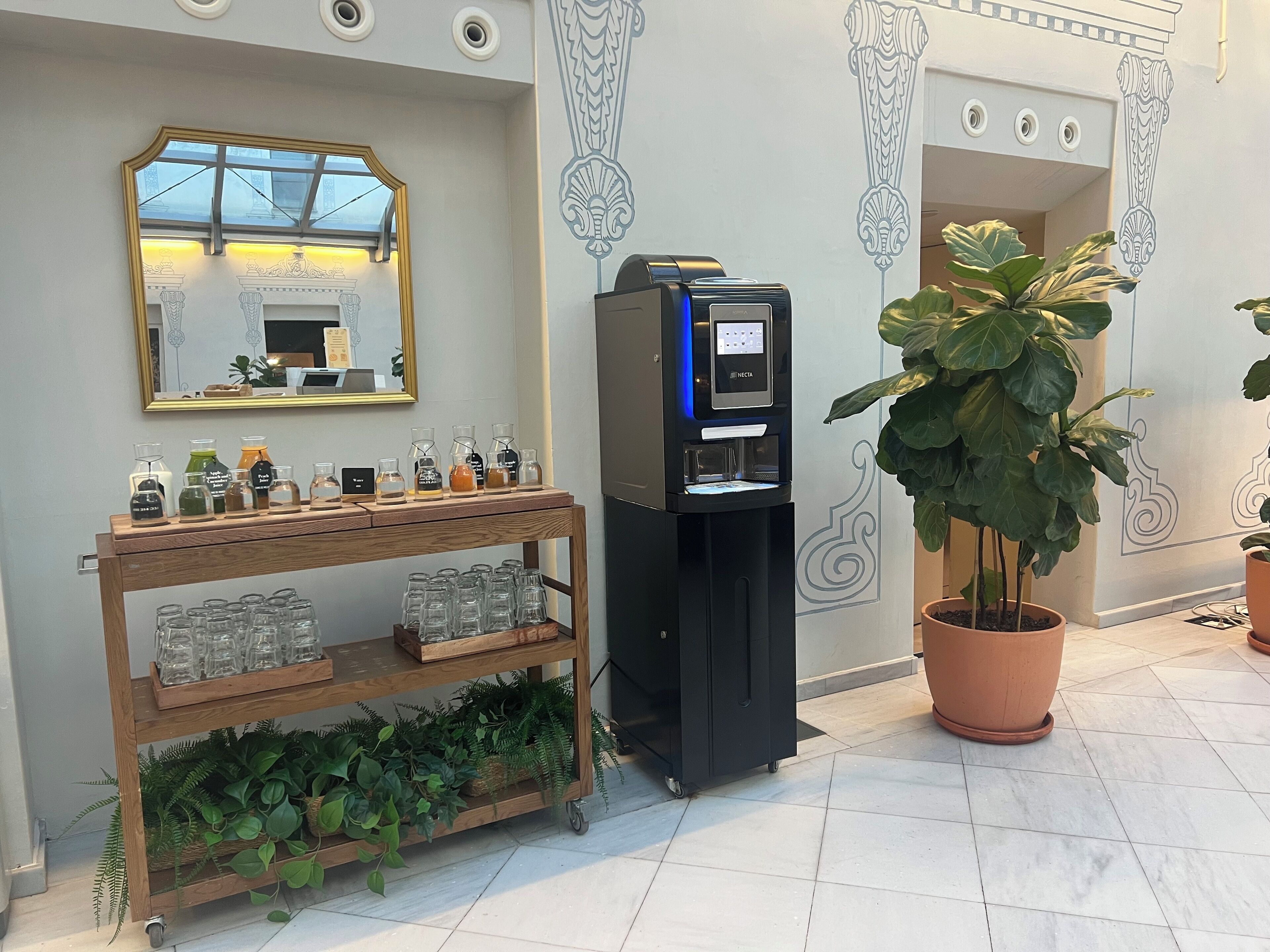 Una estación de café con una máquina expendedora, una vitrina de café y un carrito de madera con cristalería.