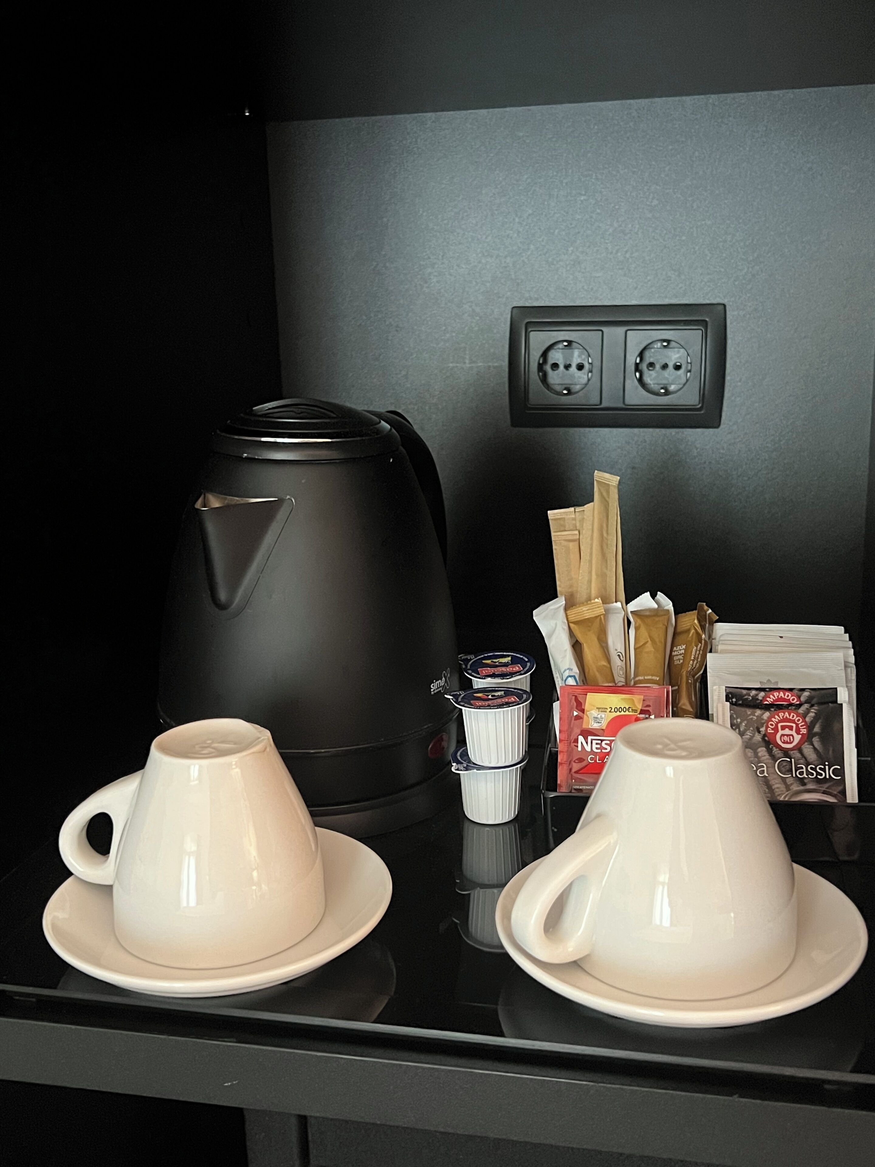A coffee station with two cups, a coffee maker, and coffee pods.