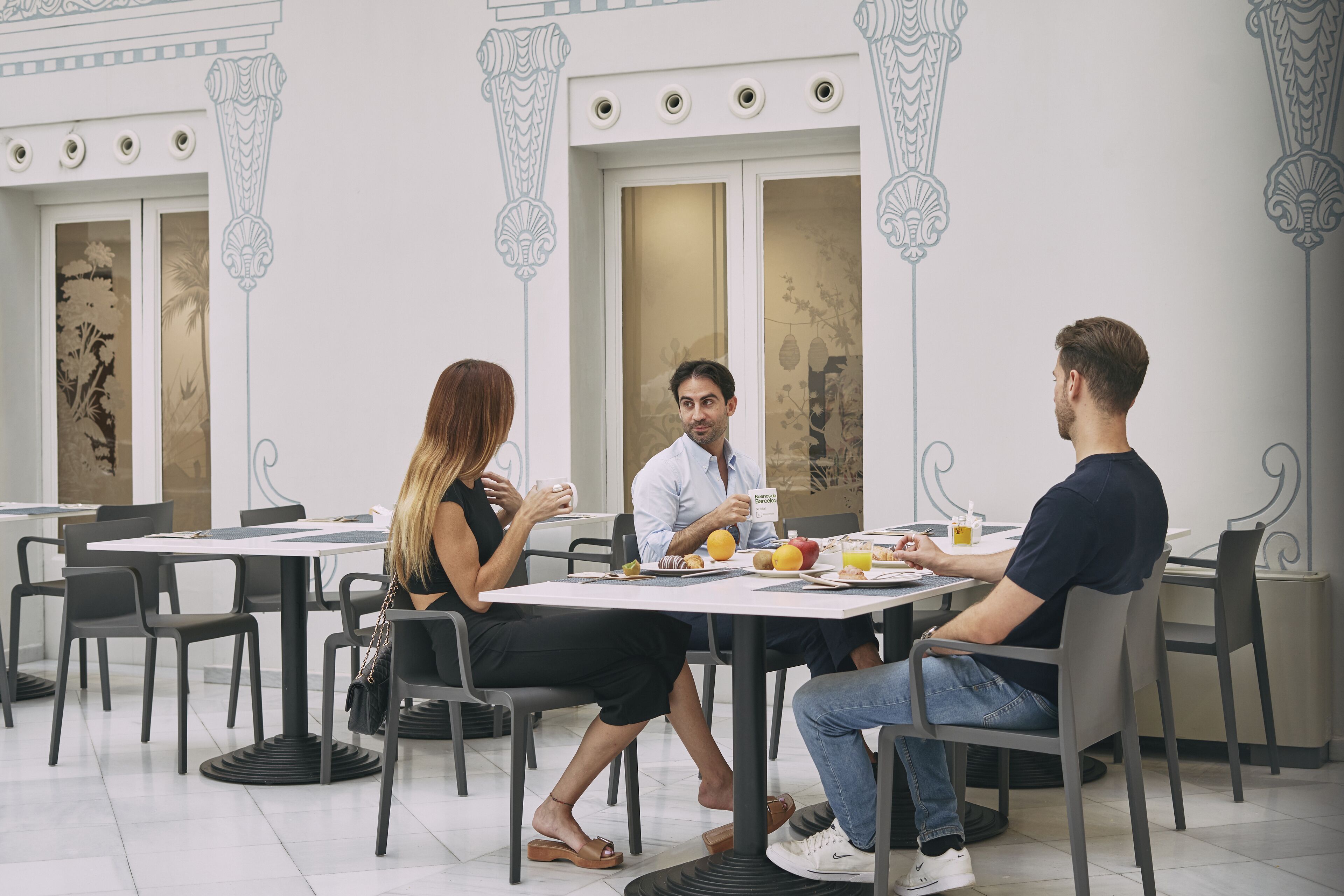 Un comedor con mesas y sillas, una persona caminando y otra sentada en una mesa.