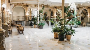 Un lobby amplio con columnas ornamentadas, plantas en macetas y un candelabro.