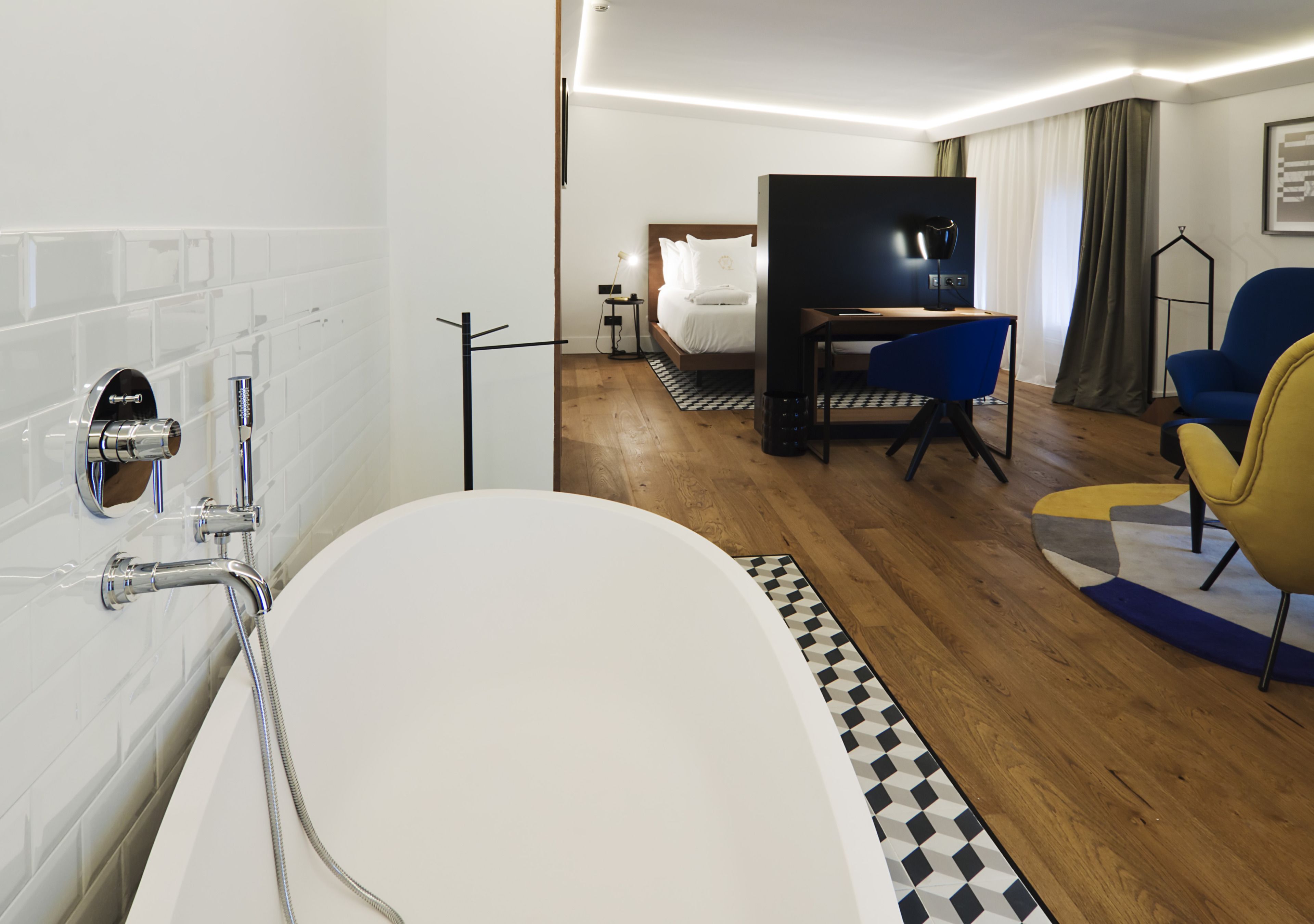 Una habitación de hotel moderna con una bañera grande, una cama con sábanas blancas, un escritorio con una silla y un televisor.