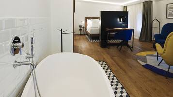 Una habitación de hotel moderna con una bañera grande, una cama con sábanas blancas, un escritorio con una silla y un televisor.