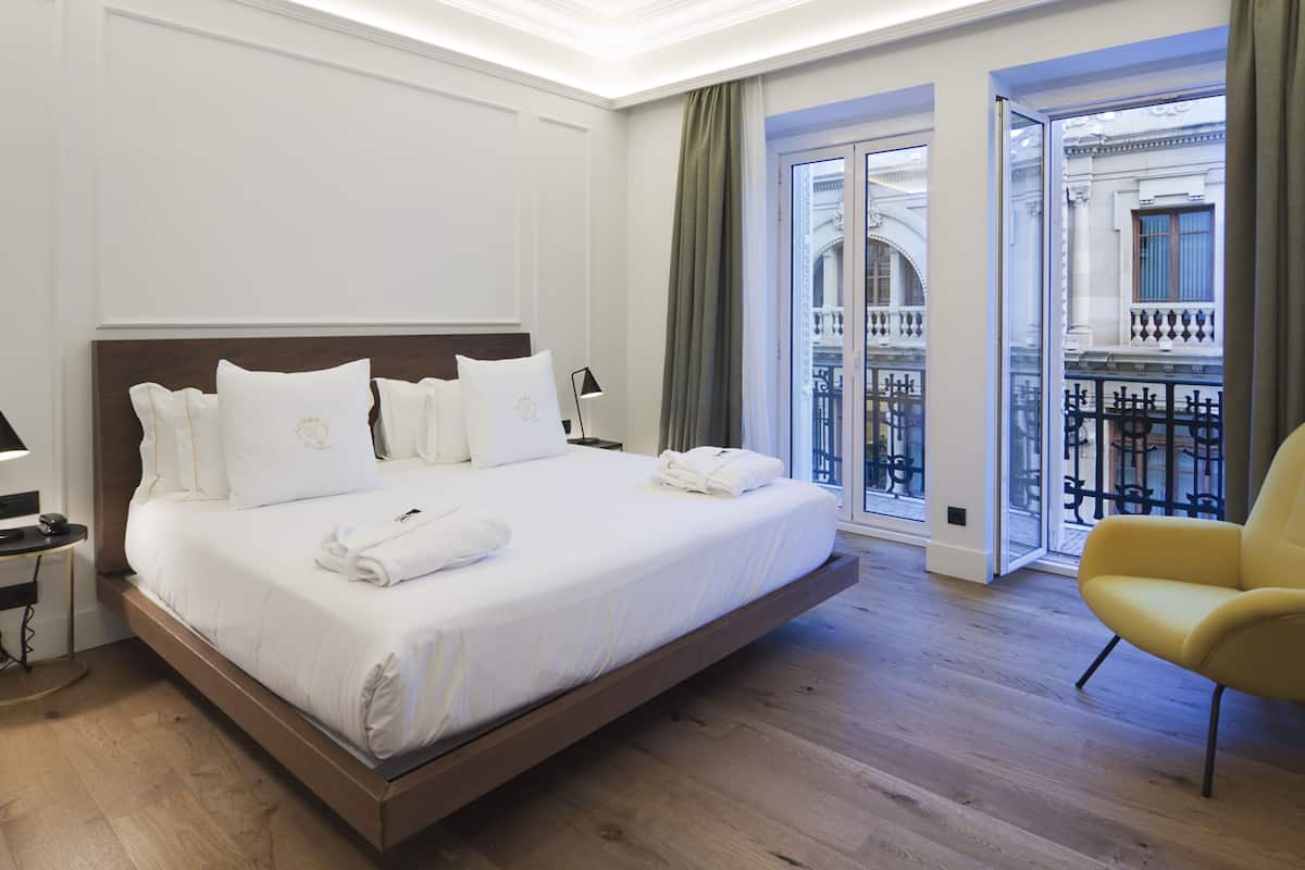 A large bed with white linens, a bedside table with a lamp, and a yellow armchair.