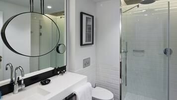 Un baño moderno con un espejo grande, un lavabo, un inodoro y una ducha con mampara de vidrio.
