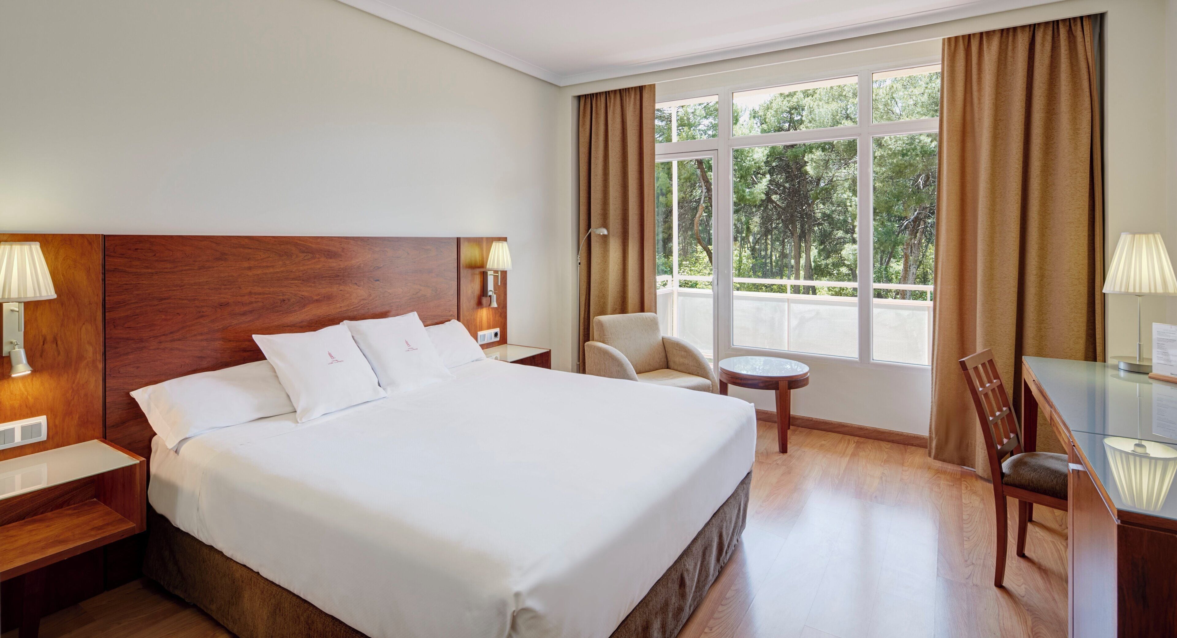 Una camera d'albergo con un letto grande, una scrivania, una sedia, un tavolino e una finestra con tende.