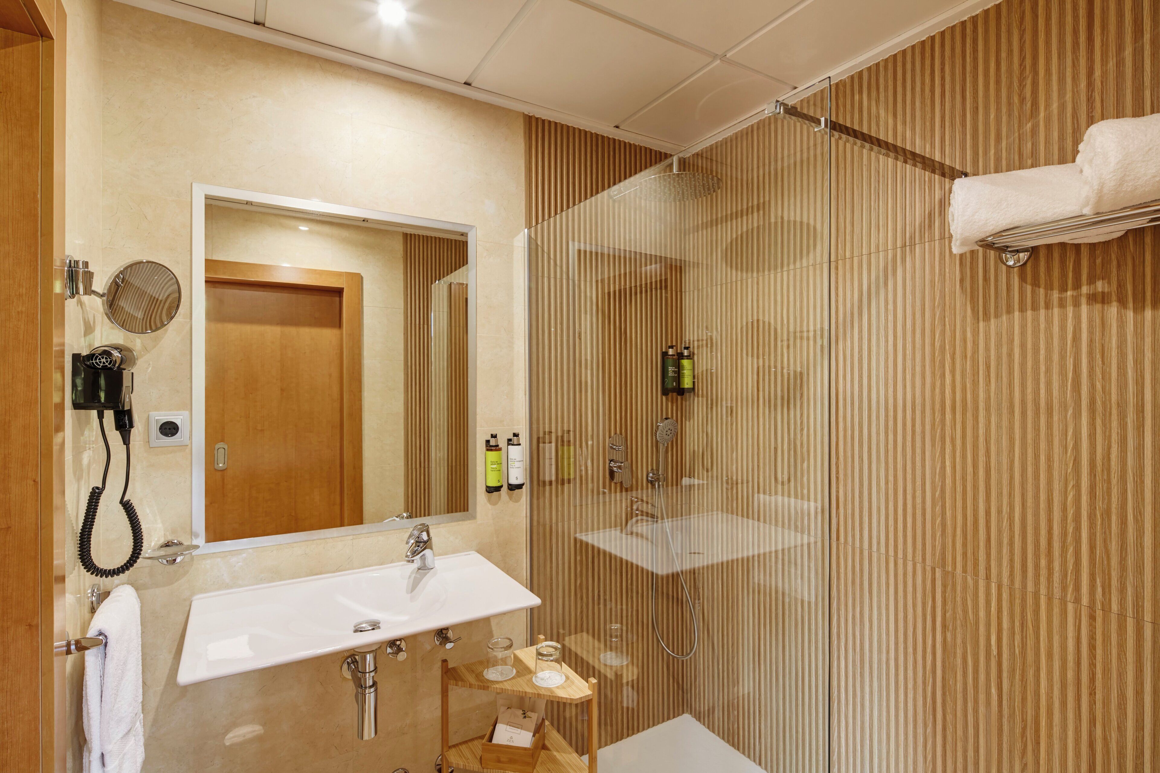 Un baño moderno con cabina de ducha de vidrio, un lavamanos y un secador de pelo.