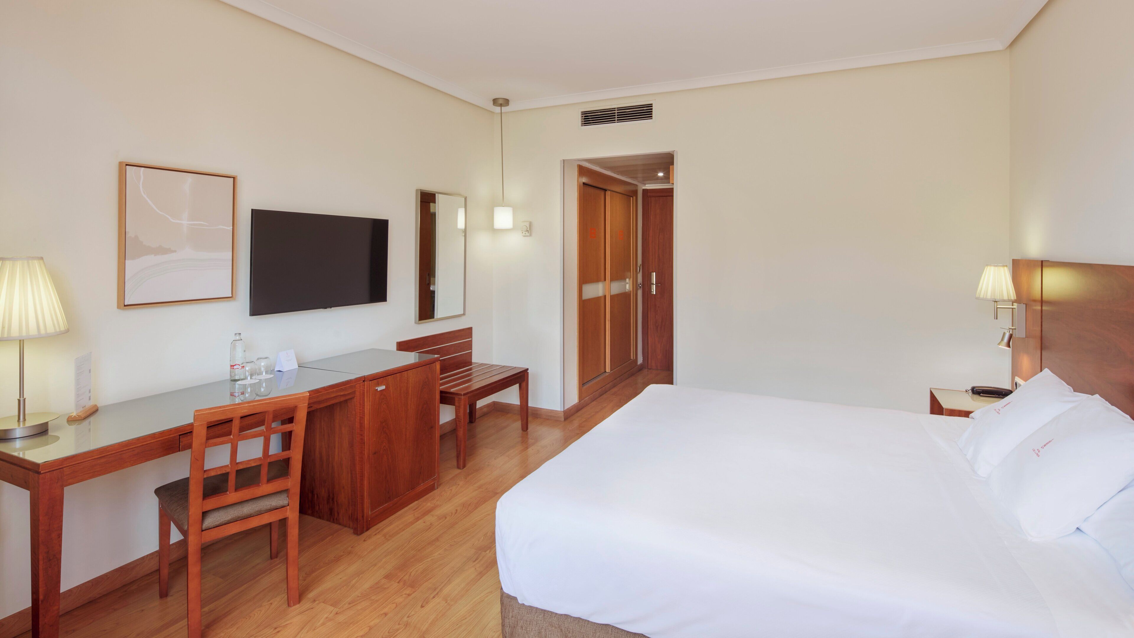 Habitación de hotel con cama, escritorio, silla, televisor y armario.