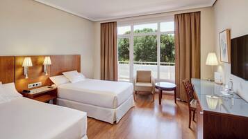 Habitación de hotel con dos camas, un escritorio, una silla, un televisor y ventanas amplias con cortinas.