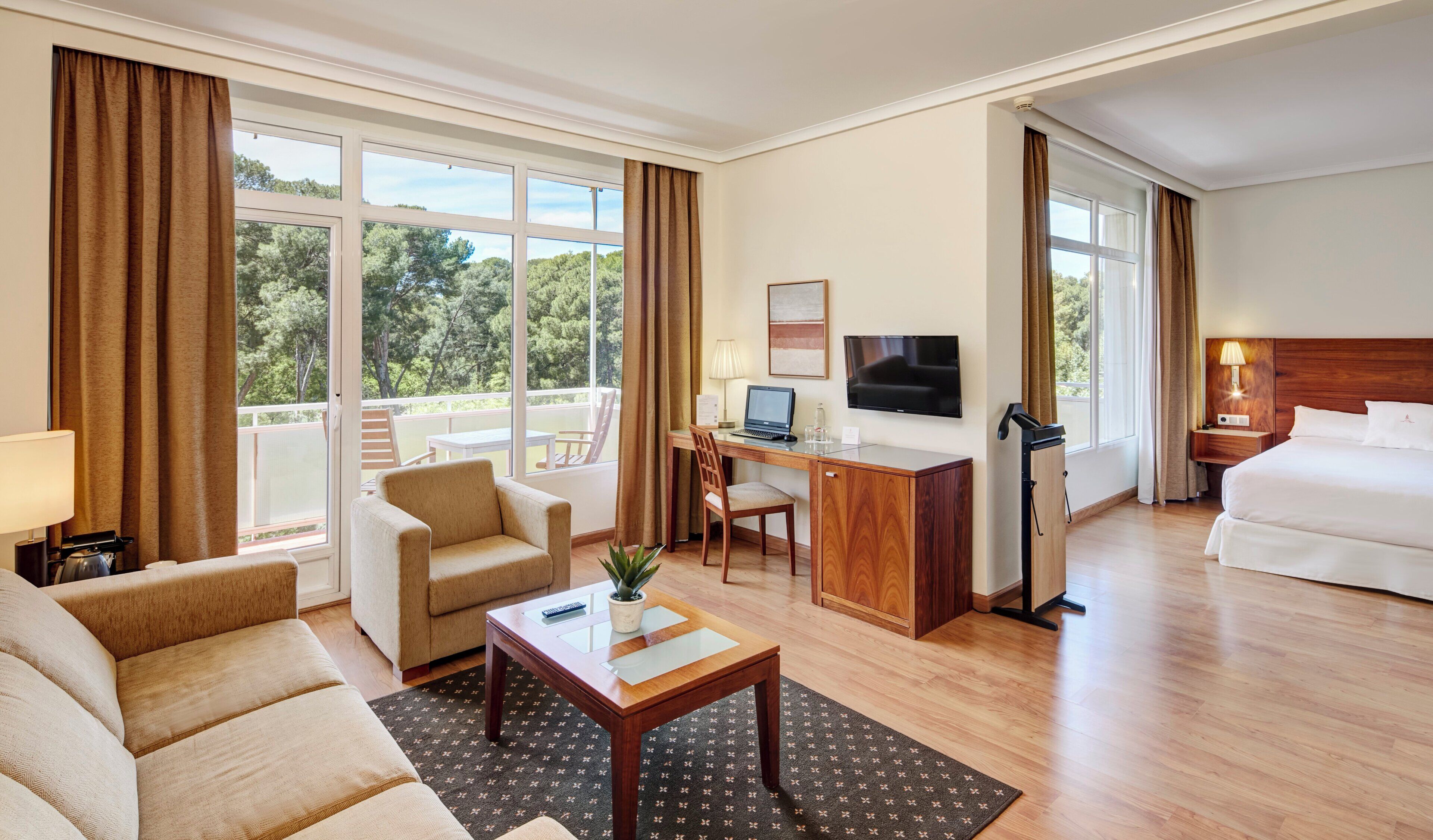 A hotel room with a bed, a desk with a computer, a TV, a sofa, and a chair.