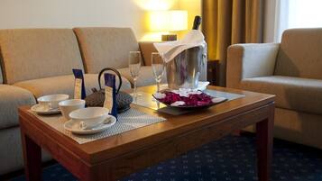 Habitación de hotel con una mesa de centro de madera, dos sofás, una lámpara, una botella de champán y una bandeja con copas y un florero.